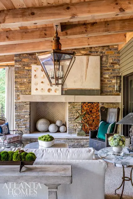 Covered porch living area with stone fireplace, wood-beamed ceiling, large lantern, and comfortable seating.