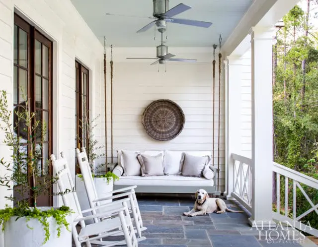 Covered porch with white rocking chairs, a swing bed, and a yellow lab dog lying on the slate floor.