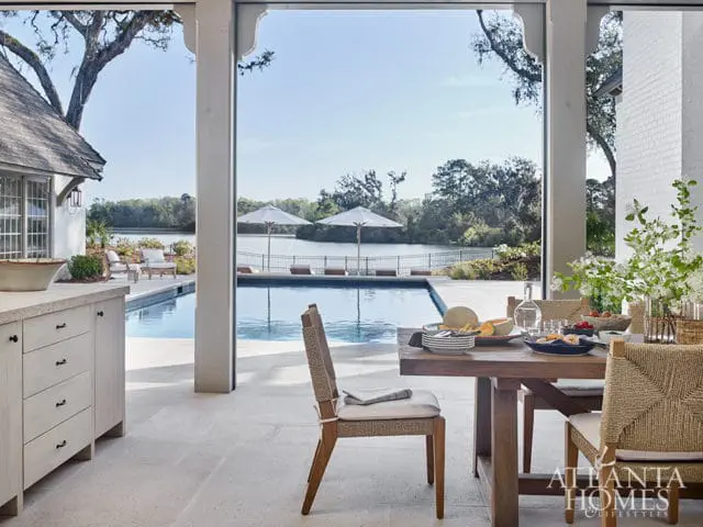 Outdoor dining area with a wooden table set for a meal, overlooking a swimming pool and lake.