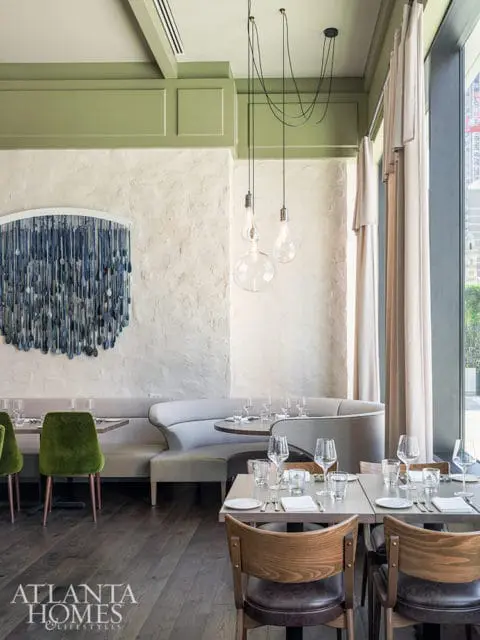 Restaurant dining area with green velvet chairs, curved banquette seating, and tables set with glassware and flatware.