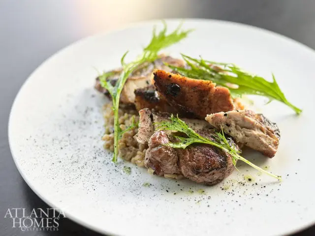Sliced grilled meat served over grains and garnished with fresh greens, with a subtle dusting of black pepper on a white plate.