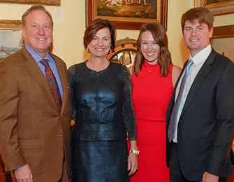 Two couples pose for a photo in an indoor setting with paintings on the wall behind them.
