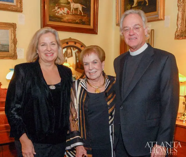 Three people posing for a photo in an interior setting with artwork on the walls and antique furniture.