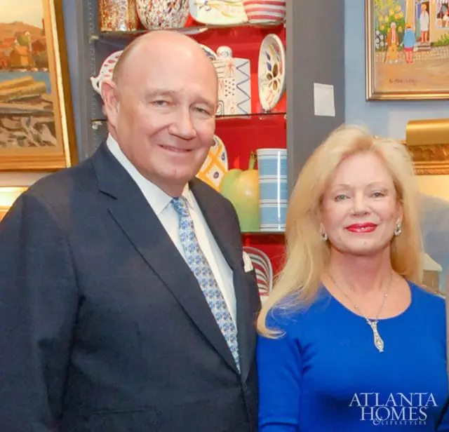 Man and woman posing in front of a shelf filled with decorative pottery.