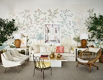 Living room with a large botanical wallpaper, white sofa, two white armchairs, a rattan chair, and a framed artwork of an interior architectural scene.