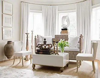Living room with white upholstered seating, a white lacquer coffee table topped with books and a crown, and tall decorative candlesticks.