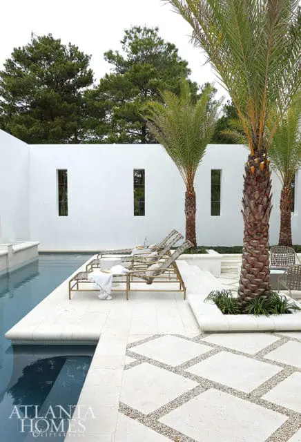 Modern white stucco courtyard with a swimming pool, chaise lounges, palm trees, and geometric stone patio