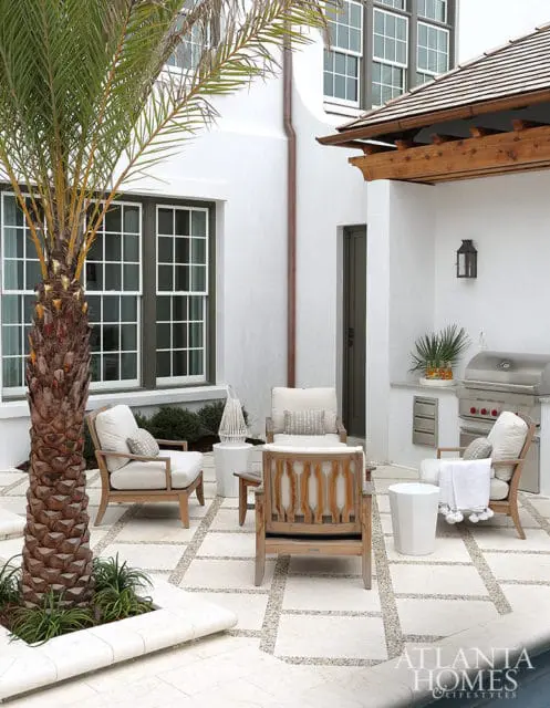 White stucco courtyard with a built-in grill, outdoor seating, and a palm tree. The patio features a stone and gravel paver pattern.
