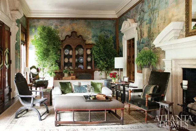 Living room with a large wooden cabinet filled with plates, a white sofa with green velvet pillows, and a landscape mural on the walls.
