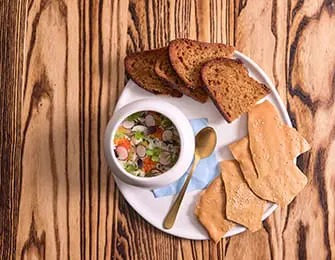 Bowl of soup with garnishes, served with toast and crackers on a white plate atop a wooden table.