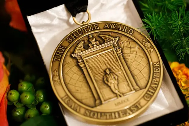 Close-up of a bronze "The Shutze Award ICAA Southeast Chapter" medal with a depiction of a figure entering a classical doorway.