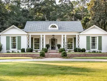 White brick house with green shutters, a covered porch with white columns, and a manicured lawn.