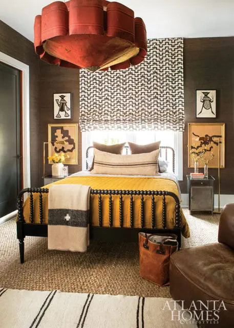 Bedroom with dark textured walls, a black spindle bed with yellow quilt, and a large red drum-shaped chandelier.