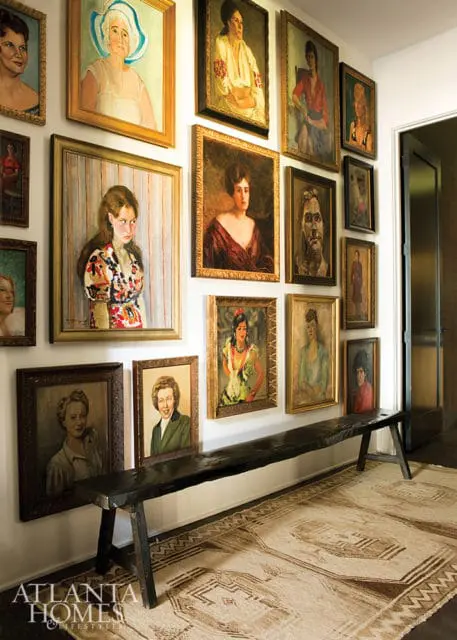 Hallway with a collection of framed oil portraits of women on the wall above a dark wood bench and a patterned rug.