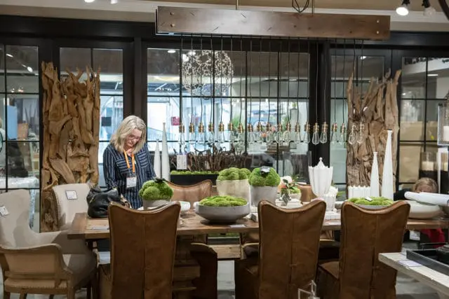 Woman in striped shirt examines moss-topped decor on a wooden dining table with leather chairs and decorative driftwood.