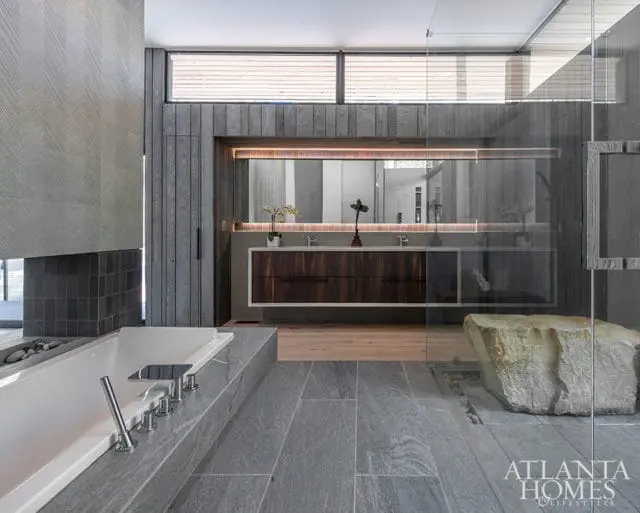 Modern bathroom with a freestanding tub, grey stone tile flooring, wood-paneled walls, and a floating double vanity with a large mirror.
