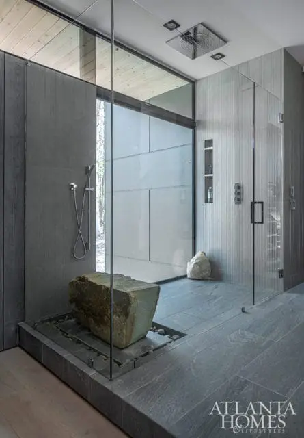 Modern bathroom with a large stone sculpture in a glass-enclosed shower, grey stone tiles, and wood-paneled walls.