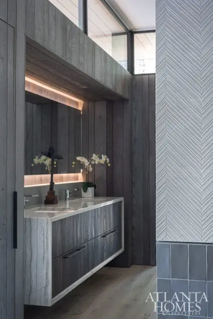 Modern bathroom with dark wood vanity, marble countertop, and chevron patterned wall tile. A mirror with integrated lighting reflects orchids and a decorative lamp.