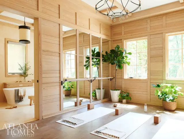 Light wood paneled yoga room with large mirrors, yoga mats, plants, and a bathtub visible in an adjacent room.