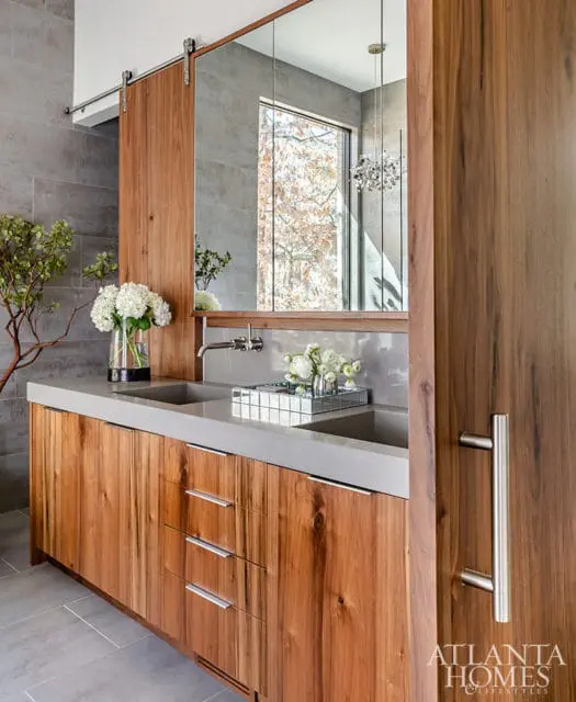 Modern bathroom with double concrete sinks, warm wood cabinetry, and a sliding barn door with a mirror