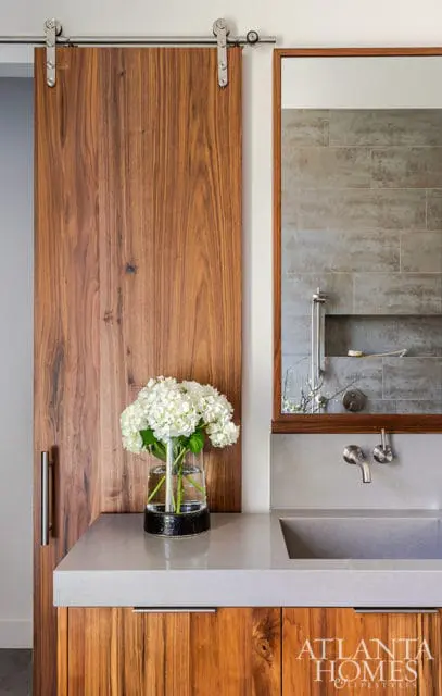 Modern bathroom with a walnut barn door, concrete countertop and sink, and a mirror reflecting a tiled shower with a niche.