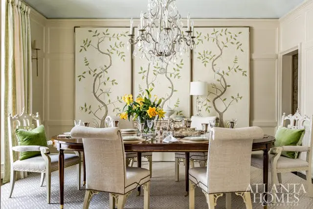 Dining room with a dark wood oval table set for a meal, upholstered chairs, a crystal chandelier, and three panels of chinoiserie wallpaper featuring trees and birds.