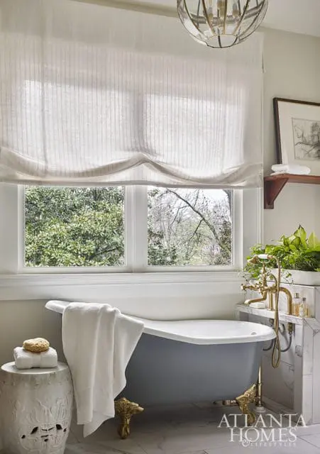 Gray clawfoot bathtub with brass fixtures, white towels on a garden stool, and a marble countertop with plants. A logo for Atlanta Homes & Lifestyles is visible in the lower right corner.