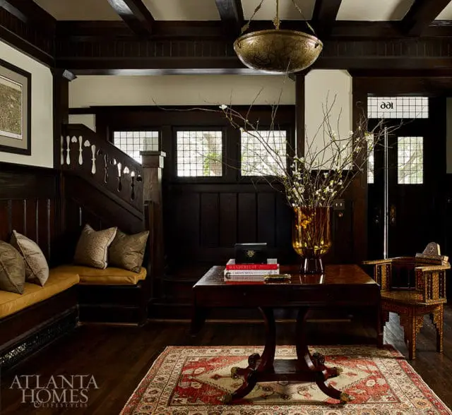 Dark wood paneled entryway with built-in bench seating, a wooden table with a vase of branches, and an ornate chair.