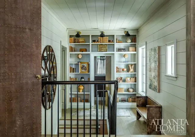 Hallway with shiplap walls and ceiling, built-in white bookshelves filled with books and decor, a dark wood bench, and a studded brown door.
