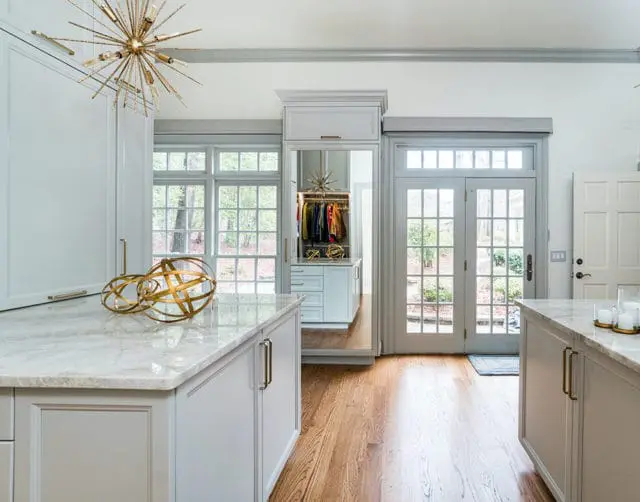 Light gray walk-in closet with marble countertops, gold sphere sculptures, and a sputnik chandelier. Double doors open to a garden view.