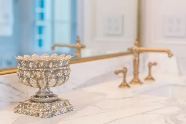 Ornate, distressed decorative bowl with gold accents sits on a marble countertop next to a gold faucet and sink.