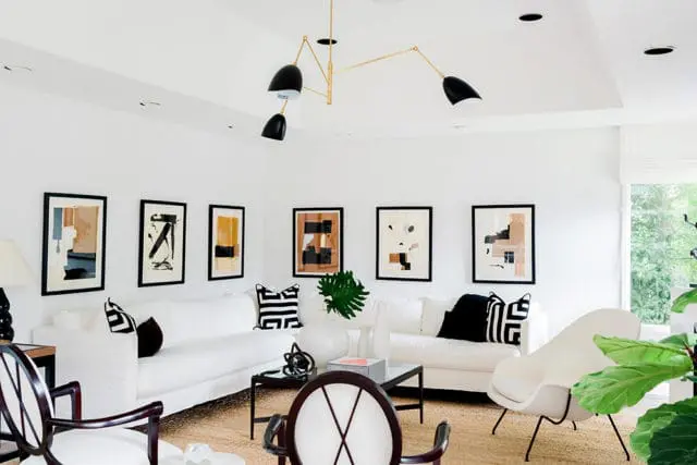 Living room with white sofas, abstract art, black and white patterned pillows, and a modern brass chandelier.