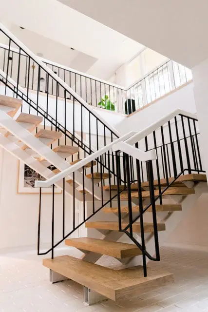 Modern staircase with light wood treads, white risers, and black metal railings. A framed artwork hangs on the white wall.