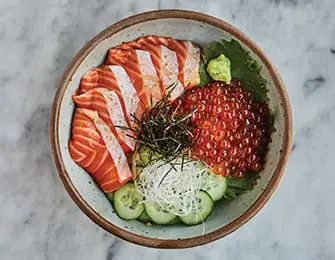 Bowl of salmon sashimi, ikura, sliced cucumber, shredded daikon, and nori garnish