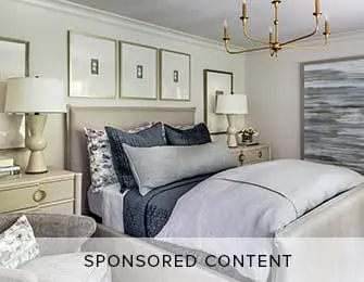 Bedroom with a king-size bed, upholstered headboard, navy blue bedding, and a gold chandelier. Three framed artworks hang above the bed.