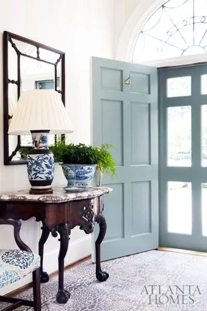Entryway with a light blue paneled door, marble-topped console table with a blue and white lamp and potted fern, and a patterned rug.