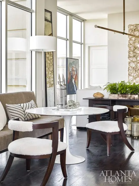 Dining area with white marble tulip table, upholstered chairs with white fur seats, and a portrait of George Washington on the wall.