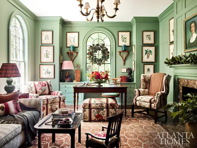 Living room with sage green walls, patterned upholstered chairs and sofa, dark wood desk, and botanical prints on walls.