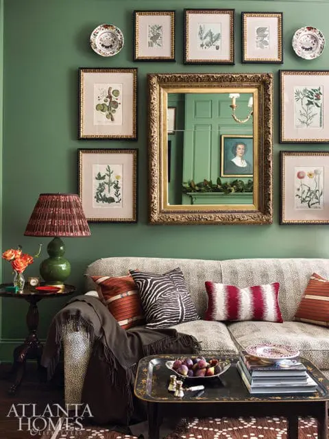 Green living room with a patterned sofa, botanical prints, a gold ornate mirror, and a dark wood side table with a lamp.
