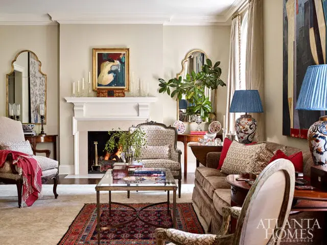 Living room with a fireplace, plush brown sofa, patterned armchairs, a glass coffee table, and ornate mirrors.