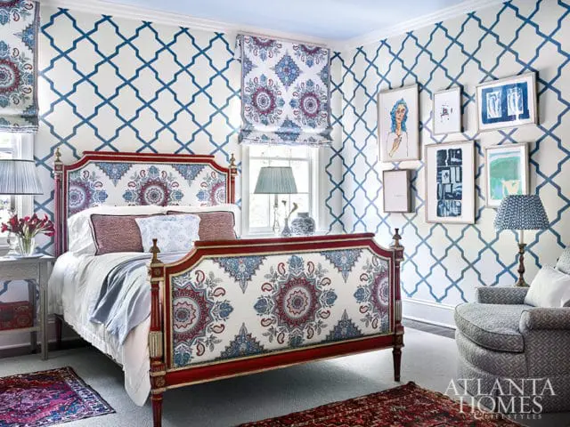 Bedroom with a red and white upholstered bed featuring a blue and red paisley pattern, blue lattice wallpaper, and framed artwork on the walls.