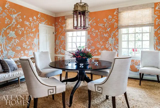 Dining room with orange floral and bird wallpaper, dark wood pedestal table with centerpiece, and upholstered chairs with nailhead trim.