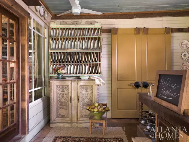 Rustic interior with a large plate rack filled with white plates, a distressed cabinet, yellow double doors, and a chalkboard sign reading 'Redline plantation'.