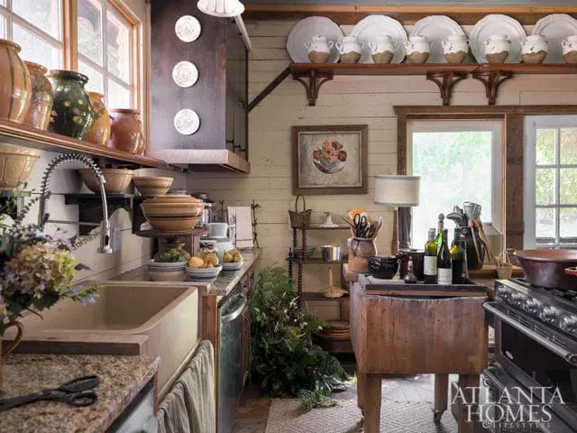 Rustic kitchen with cream-colored shiplap walls, a large farmhouse sink, granite countertops, and open shelving displaying pottery and dishes.