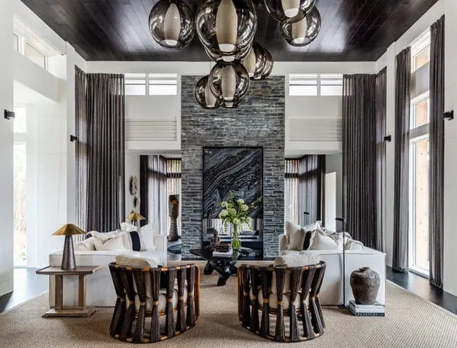 Living room with white sofas, woven armchairs, stone fireplace, and a large modern chandelier with glass globes.