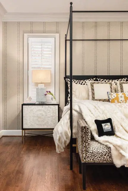 Bedroom with a black canopy bed, upholstered bench with leopard print, and a nightstand with a mother-of-pearl inlay.