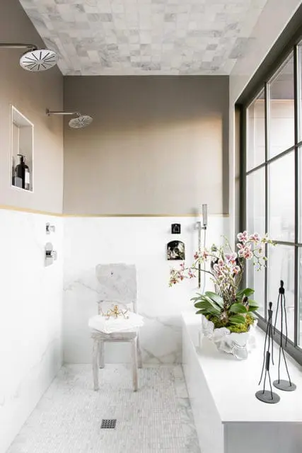 Modern bathroom with marble tile ceiling and walls, dual shower heads, and a decorative orchid plant on a windowsill.