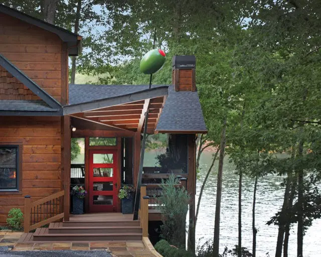 Wooden house with red front door and a large martini olive decoration on the roof, overlooking a lake