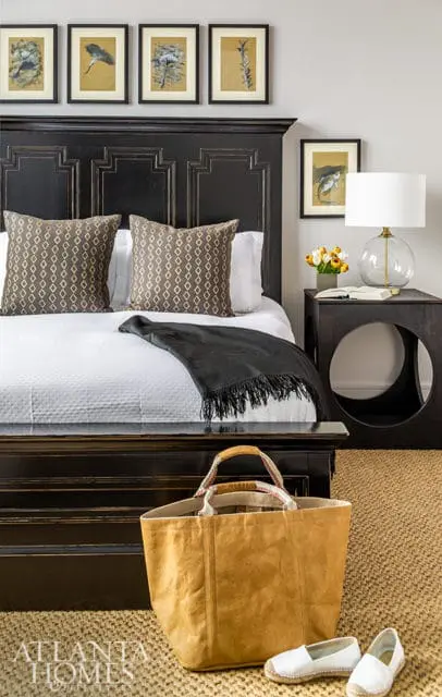 Bedroom with a dark wood ornate headboard, white quilted bedding, patterned throw pillows, and framed botanical prints above the bed.