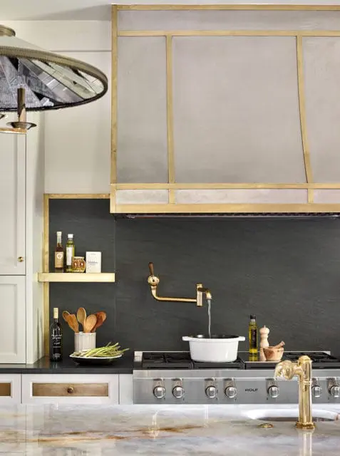 Modern kitchen with a dark slate backsplash, brass pot filler faucet, and a stainless steel range. A white pot is filling with water on the stovetop.